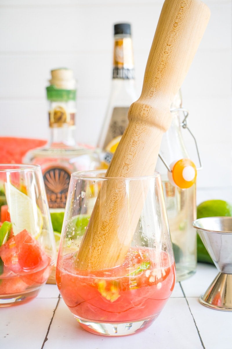 A glass filled with crushed watermelon and a muddler.