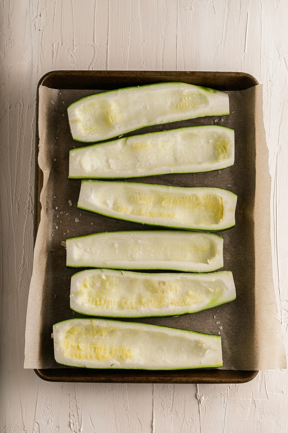 Zucchinis halved with insides scooped on a baking sheet.