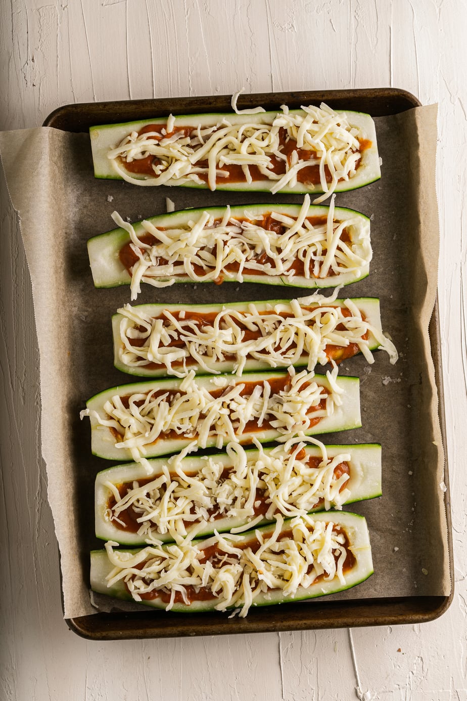 Unbaked zucchini pizza boats on a baking sheet.