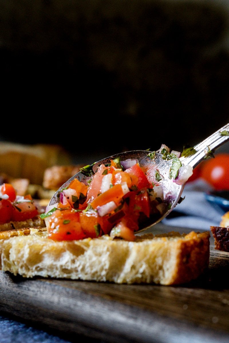 Tomato basil bruschetta mix being added to a piece of crostini