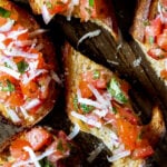 Close up of pieces of bruschetta topped with shaved parmesan on a cutting board