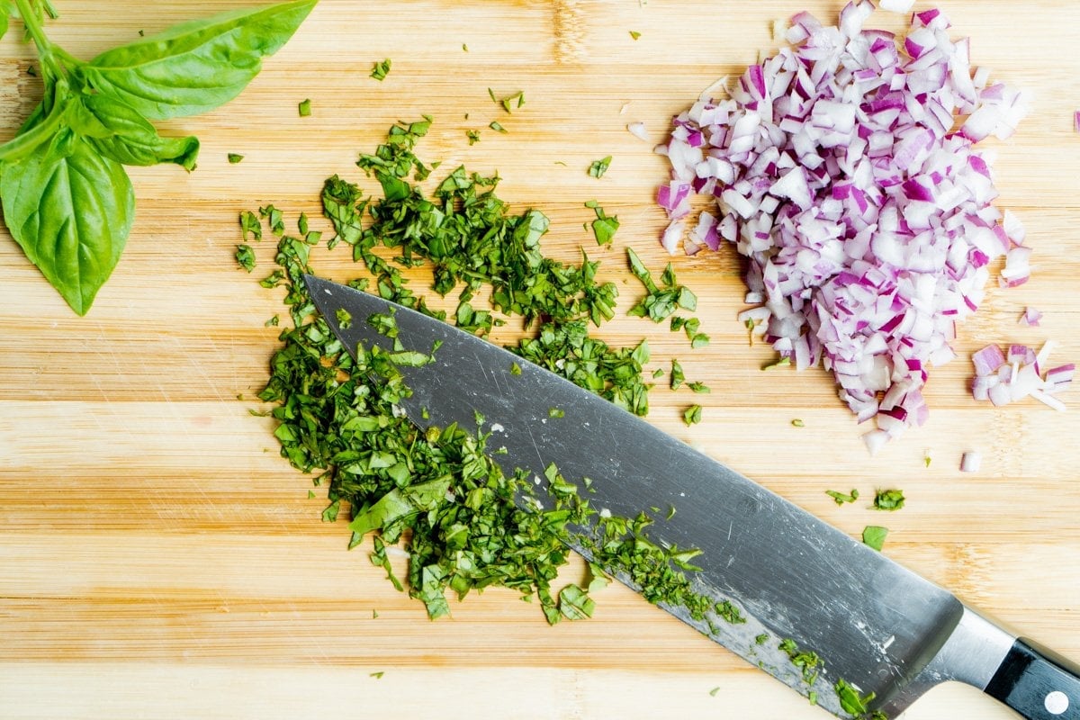 chopped basil and red onion on a cutting board with a knife