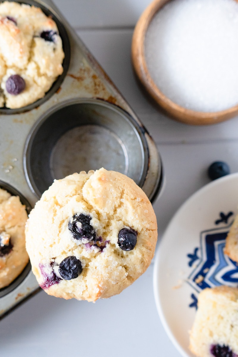 A blueberry muffin on top of a muffin tin sprinkled with coarse sugar.