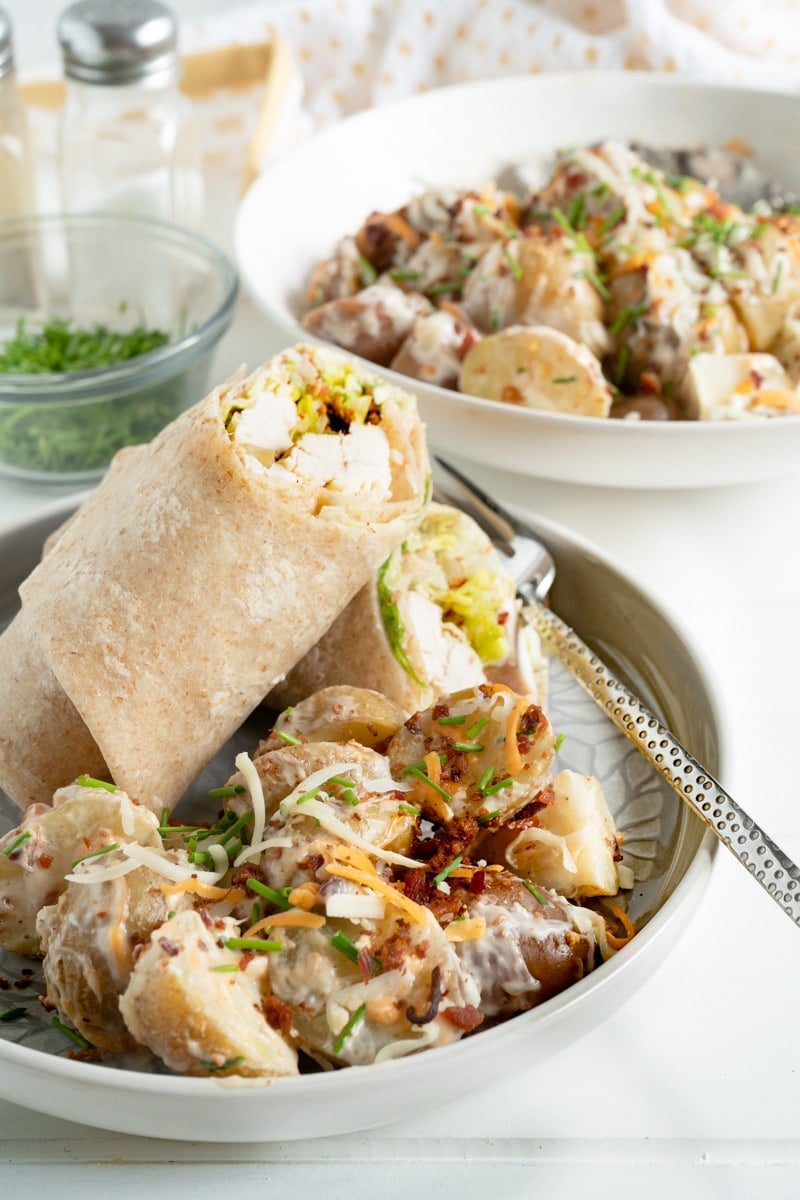 A chicken wrap on a plate with a side of potato salad