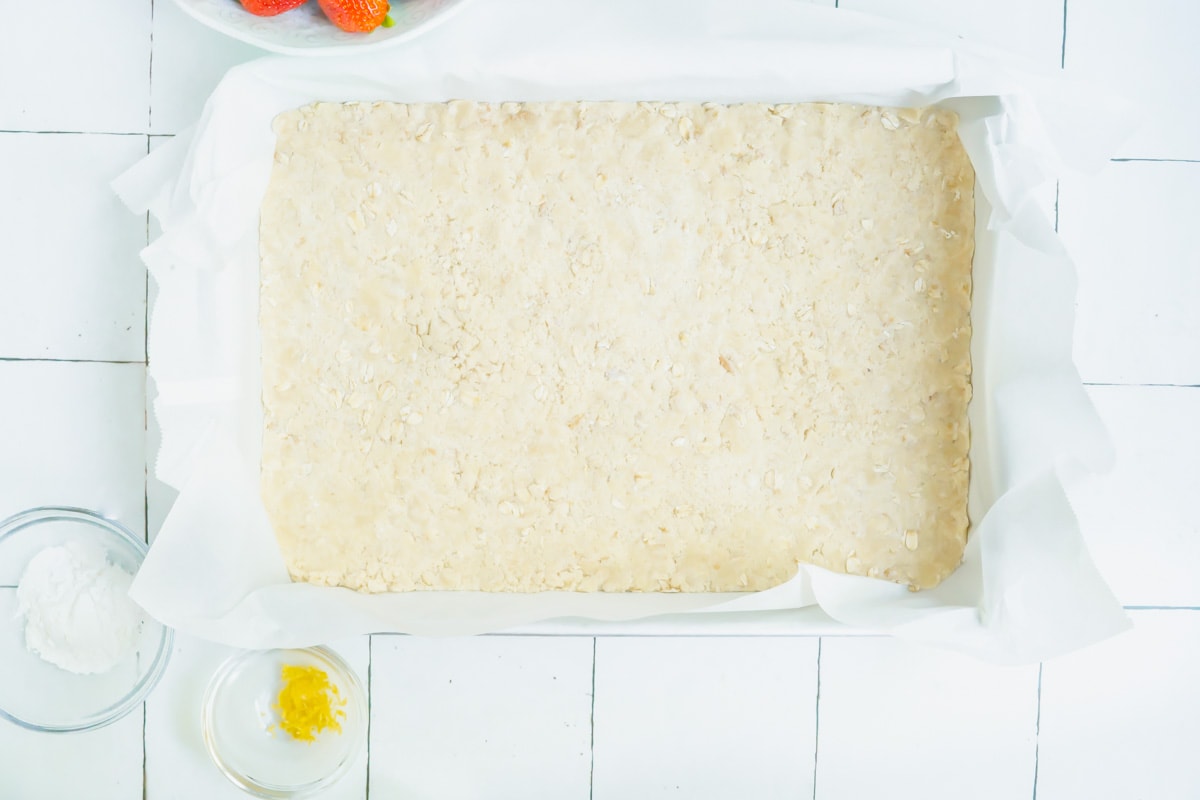 A dessert bar crust pressed into the bottom of a parchment paper lined baking dish.