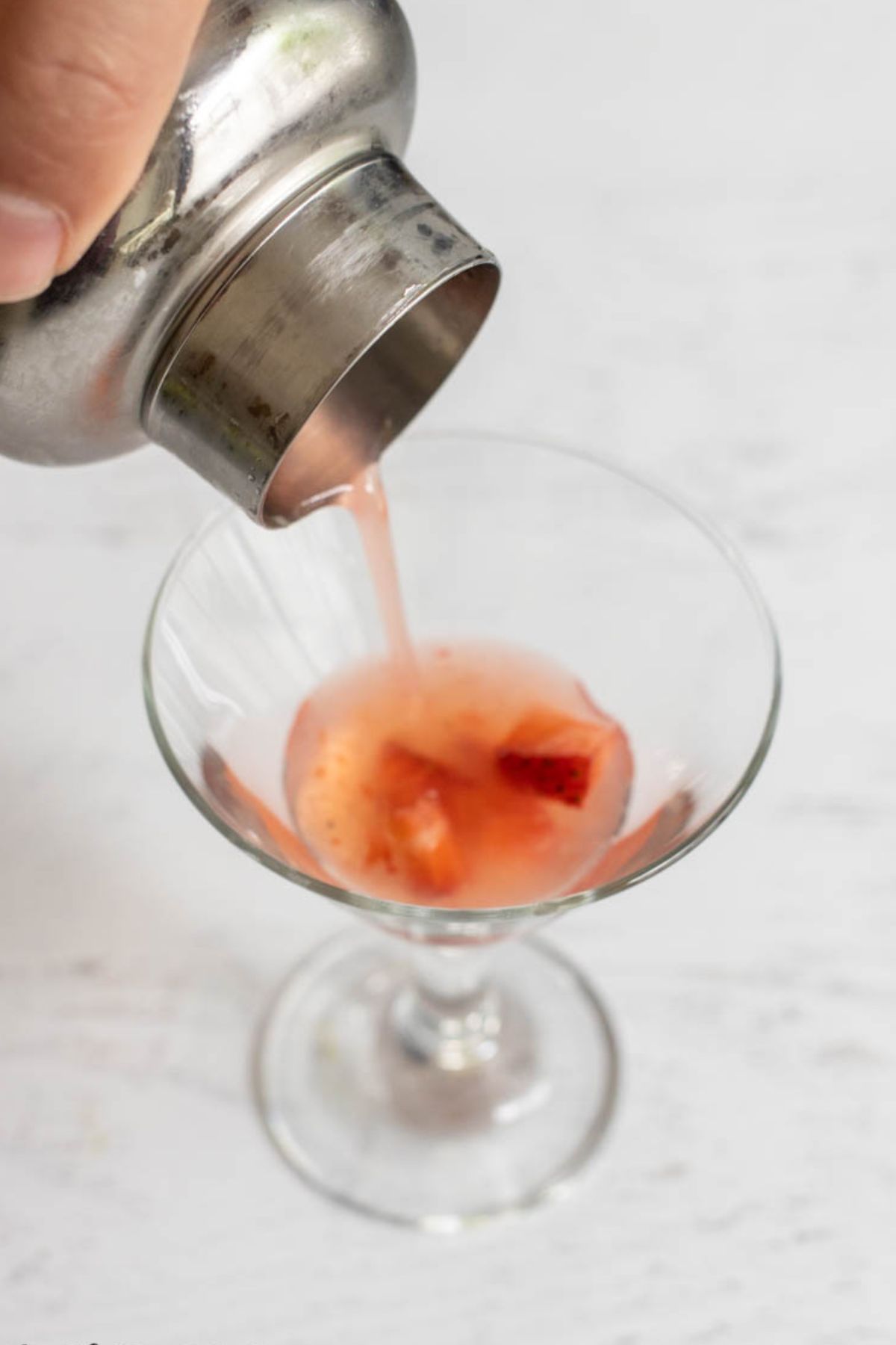 A strawberry gimlet cocktail being poured into a martini glass.