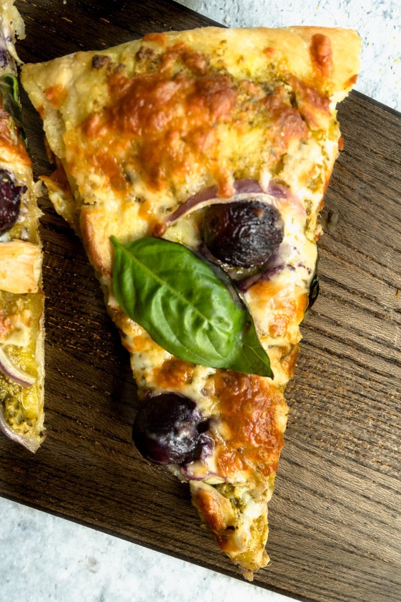 A slice of chicken pesto pizza on a cutting board.