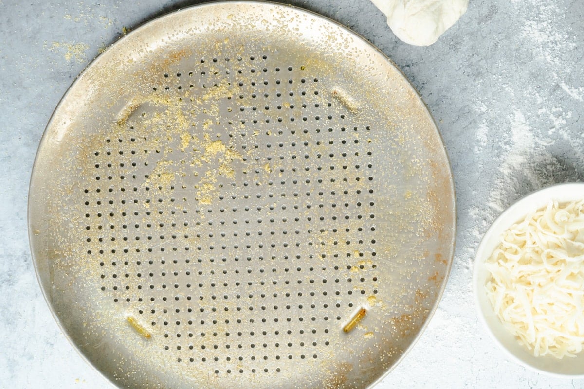 A pizza pan sprayed and coated in cornmeal