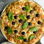 A Chicken pizza made with pesto, mozzarella, grapes and red onion and topped with basil.