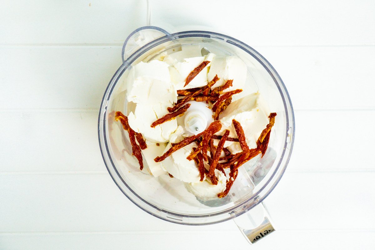A food processor with goat cheese, cream cheese and sundried tomatoes
