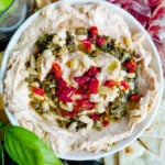 A close up of a pesto and cream cheese dip topped with sundried tomatoes and pesto