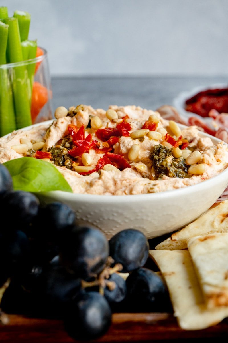 A bowl filled with a sundried tomato cream cheese spread on a charcuterie board.