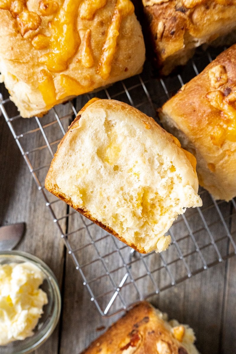 A cheese roll recipe with a baked roll in half on a cooling rack.