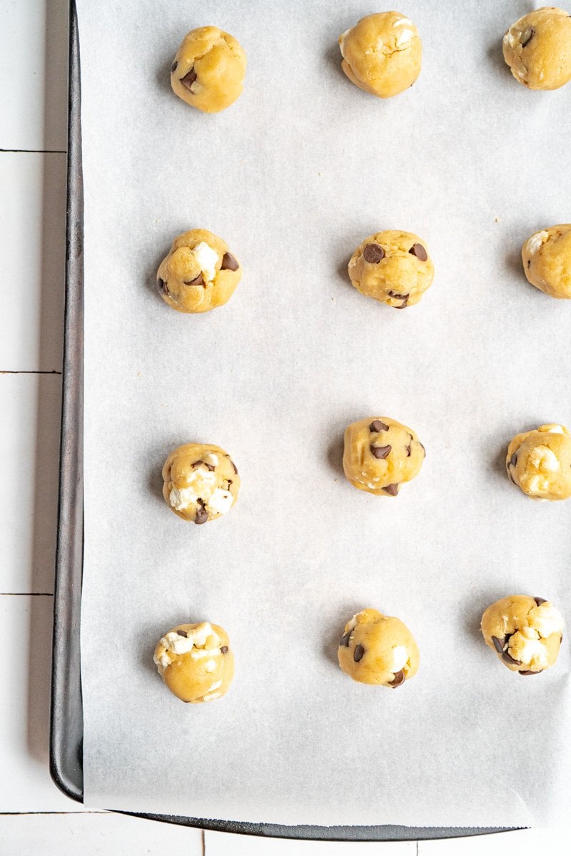 Chocolate chip marshmallow cookies rolled into balls on a baking sheet.