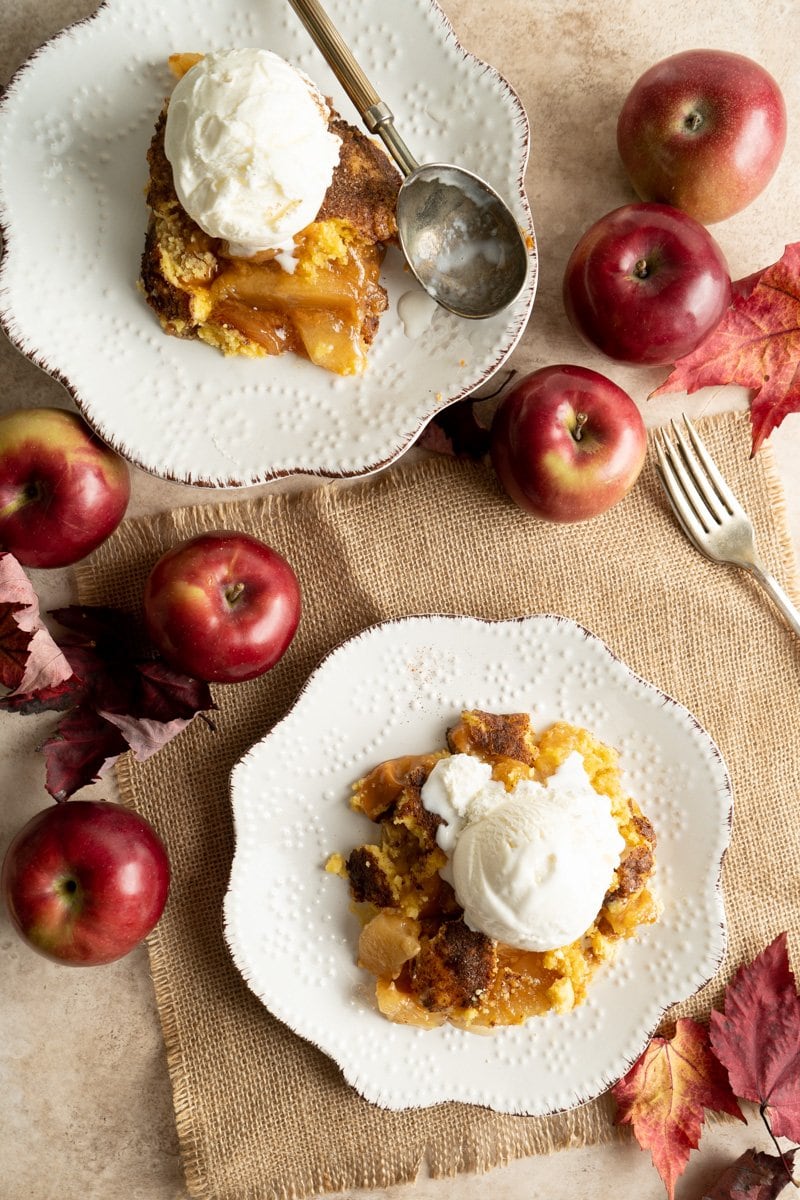 Two plates with servings of apple dump cake and ice cream surrounded by apples.