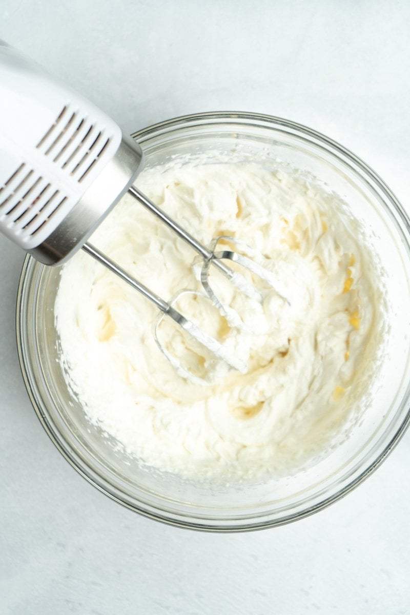 Whipped cream in a bowl with a hand mixer.