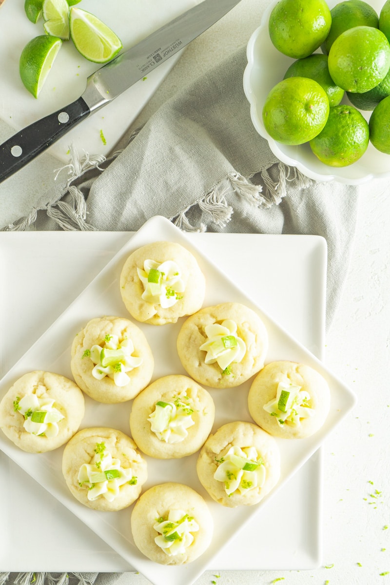 Key limed cookies filled with cream cheese on a plate with a bowl of limes.
