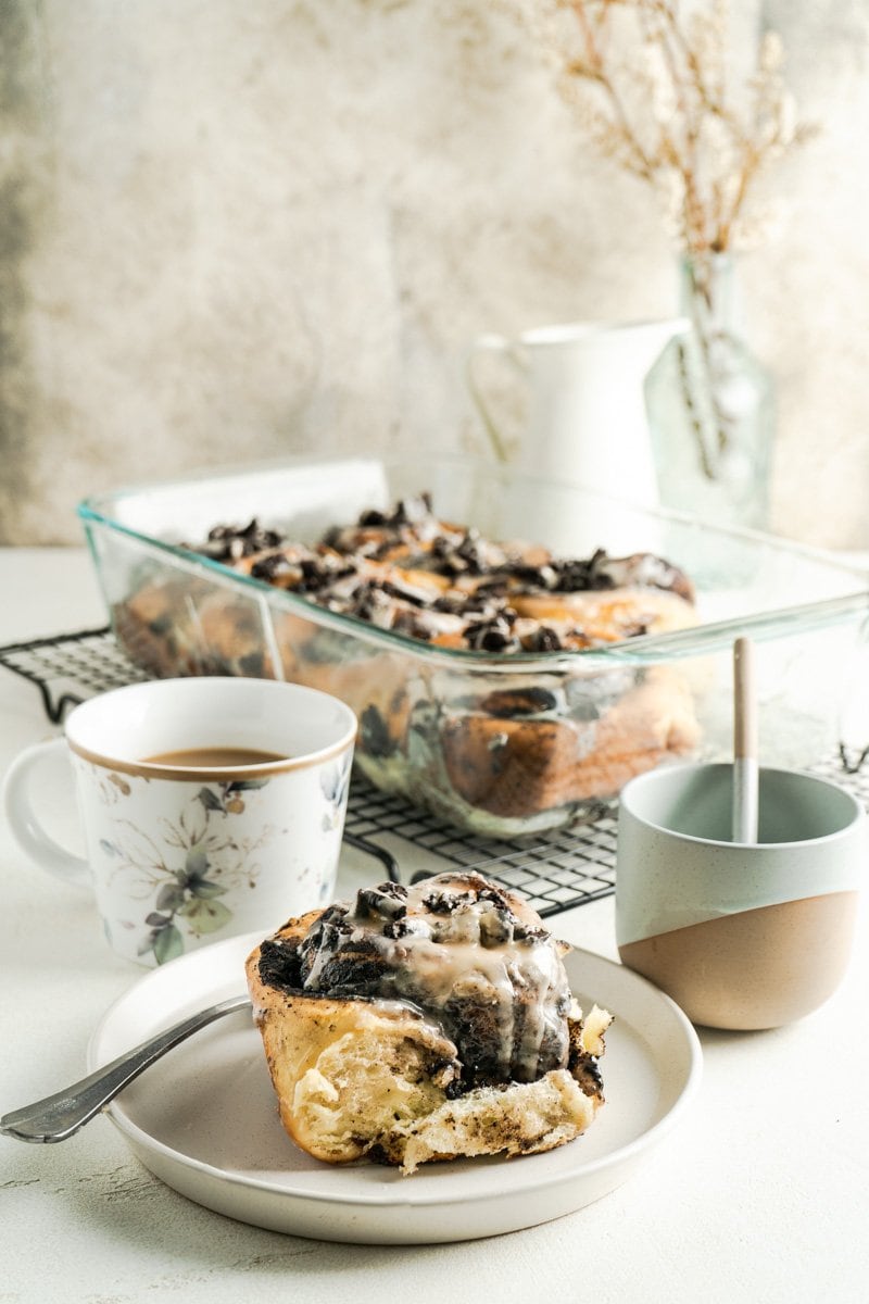 A cookies and cream cinnamon roll on a table with more in a dish.