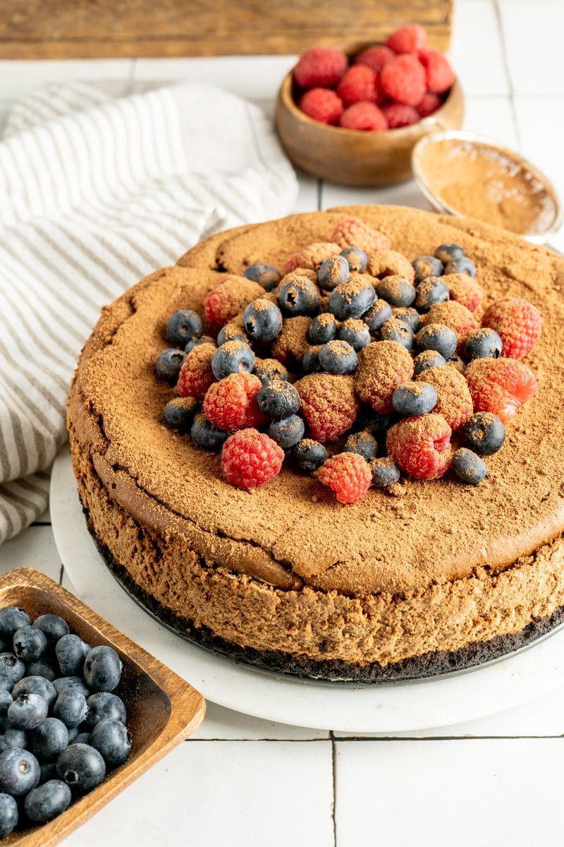 A chocolate Sicilian ricotta cheesecake recipe topped with berries on a table.