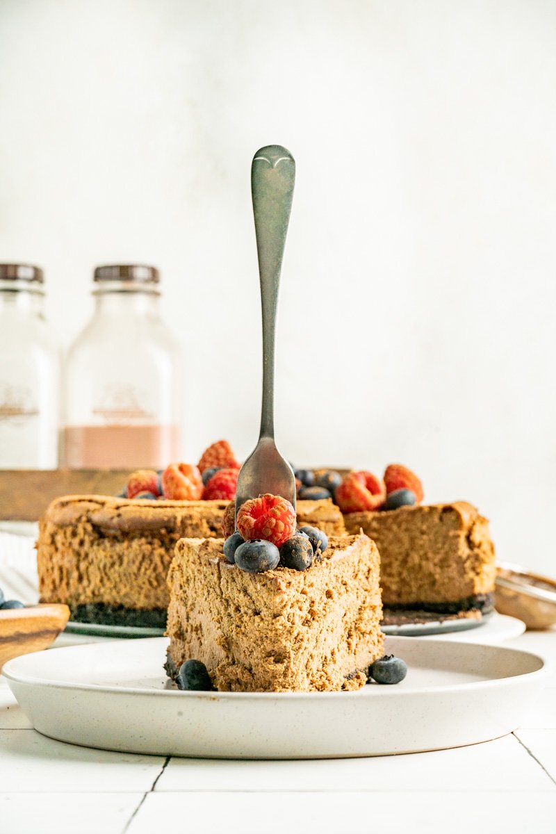 A slice of chocolate cheesecake on a plate with the full cake behind.