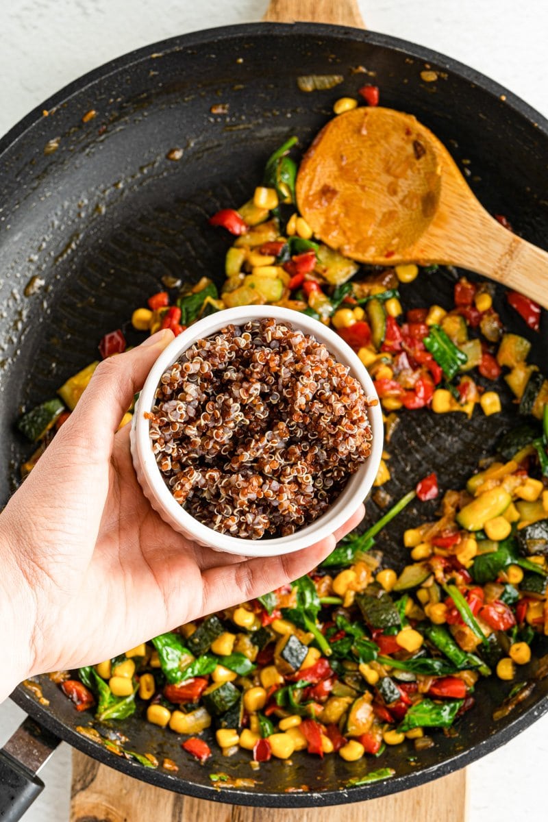 Cooked quinoa being put in a pan of veggies.