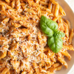 Close up of a penne vodka with chicken recipe topped with a sprig of basil.