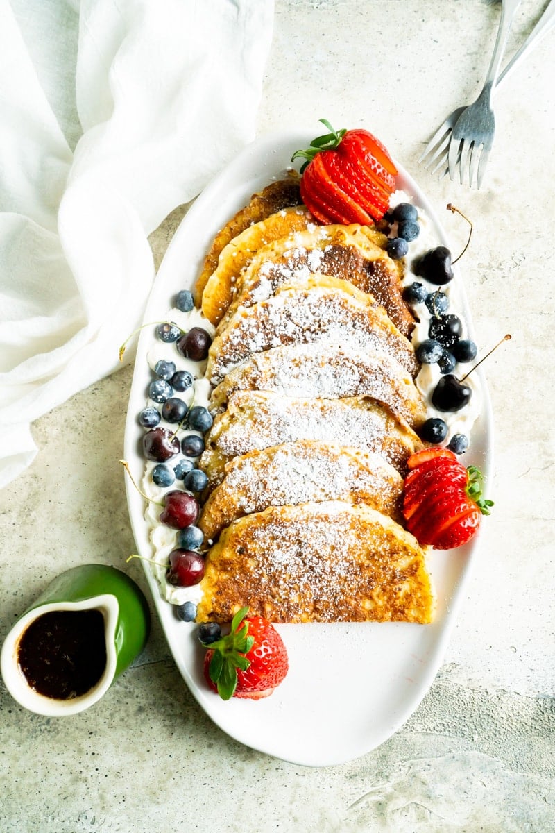 A platter of french toast made out of pancakes on a platter with berries and sugar.
