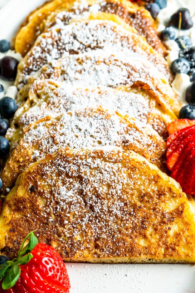 A platter of fluffy french toast made out of pancakes cut in half topped with icing sugar and berries.