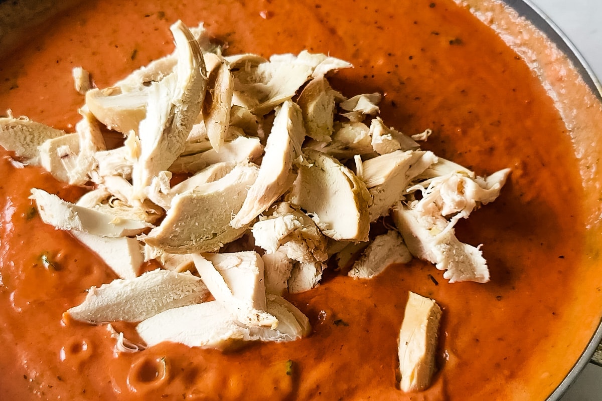 Sliced chicken breast in a pan of creamy vodka sauce.