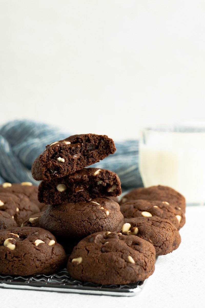 Chickpea chocolate chip cookies stacked on a cooling rack near a glass of milk.
