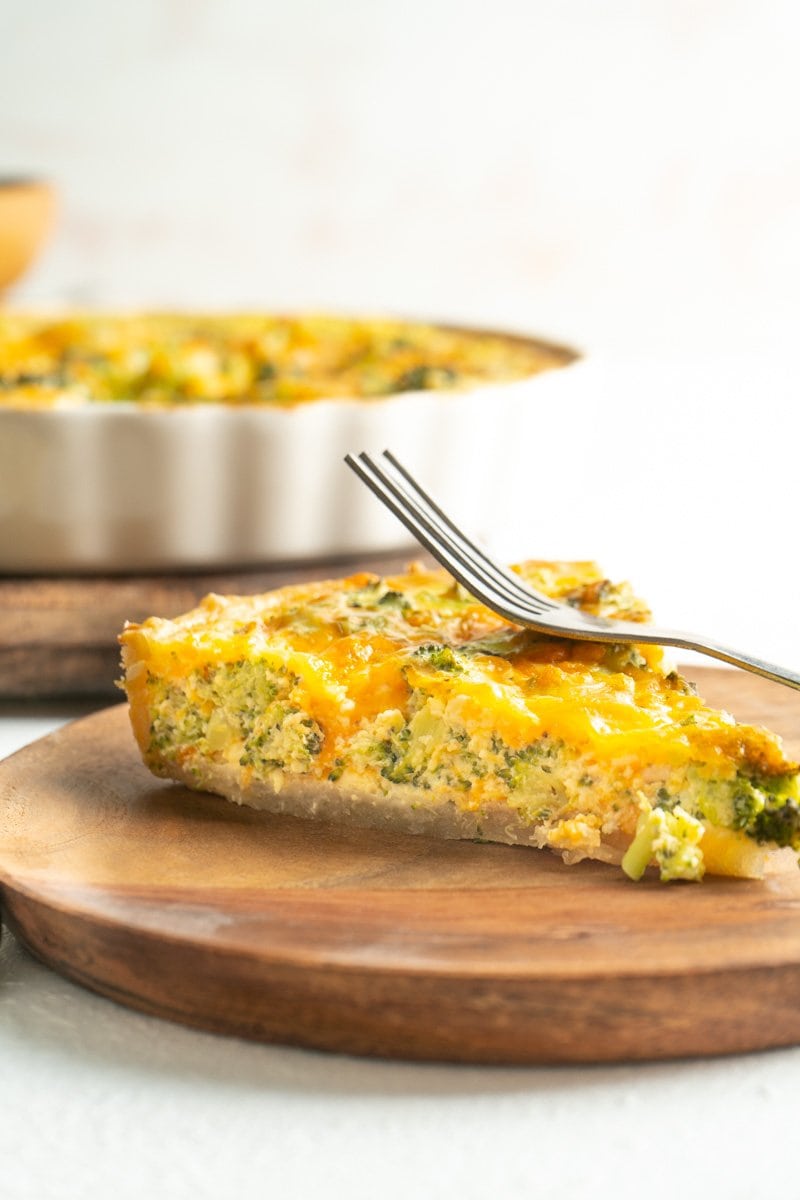 A slice of a broccoli cheddar tart on a wood plate with a fork.