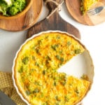 A breakfast quiche recipe on a cutting board with one slice missing.