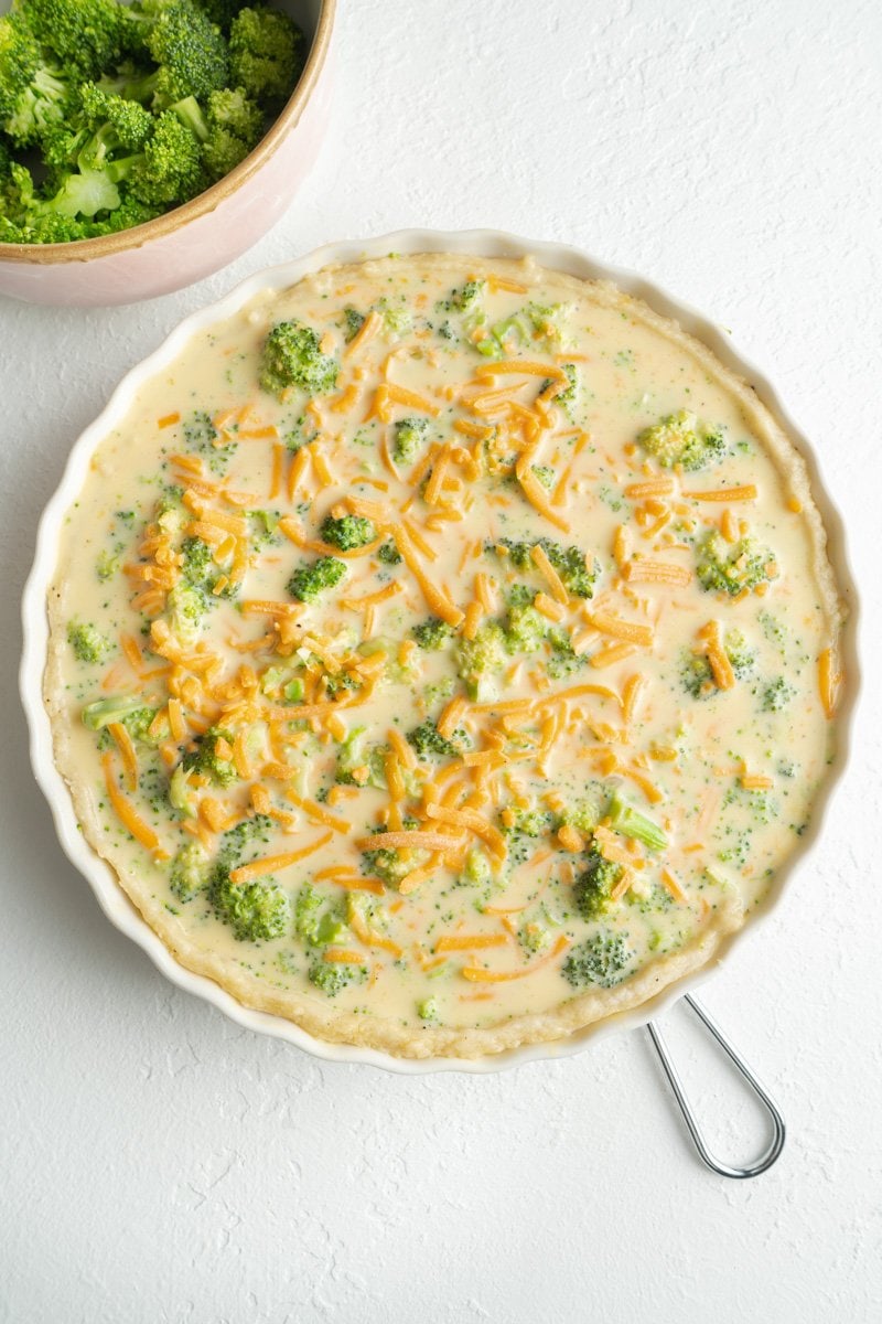 An uncooked vegetarian quiche with broccoli ready to be baked.