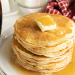 A stack of diner pancakes on a plate with butter and syrup.