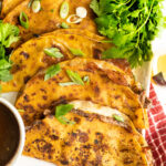 A platter or quesabirria tacos with consomme and cilantro.