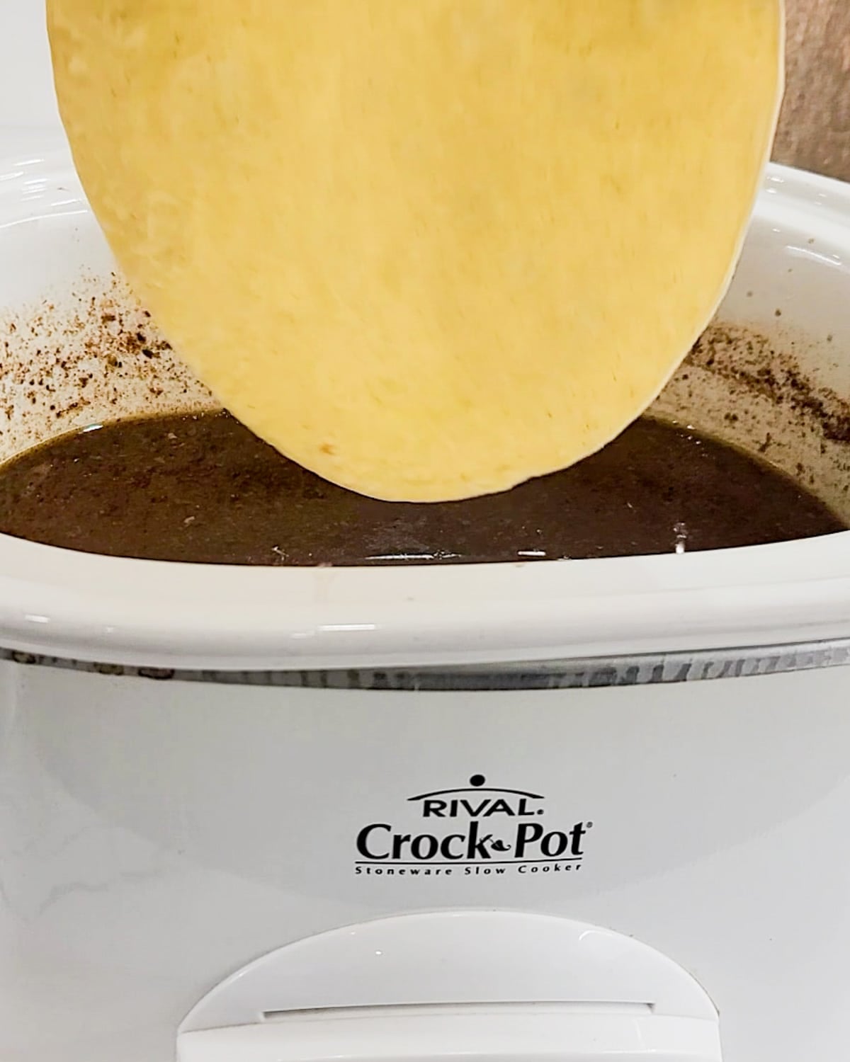 A corn tortilla being dipped in beef birria consomme.
