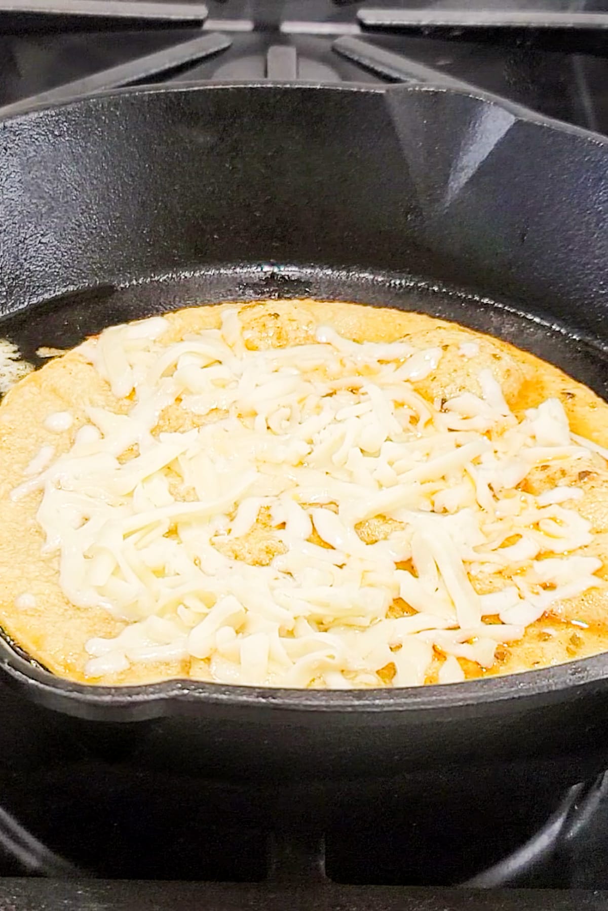 A taco shell with cheese being heated in a skillet.