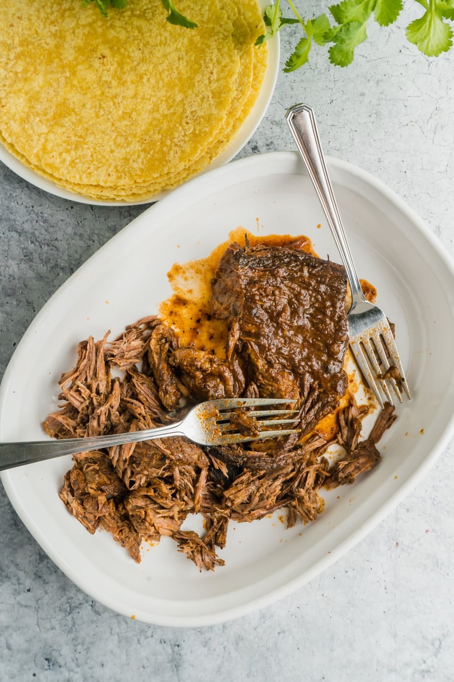Beef birria being shredded in a dish with two forks.