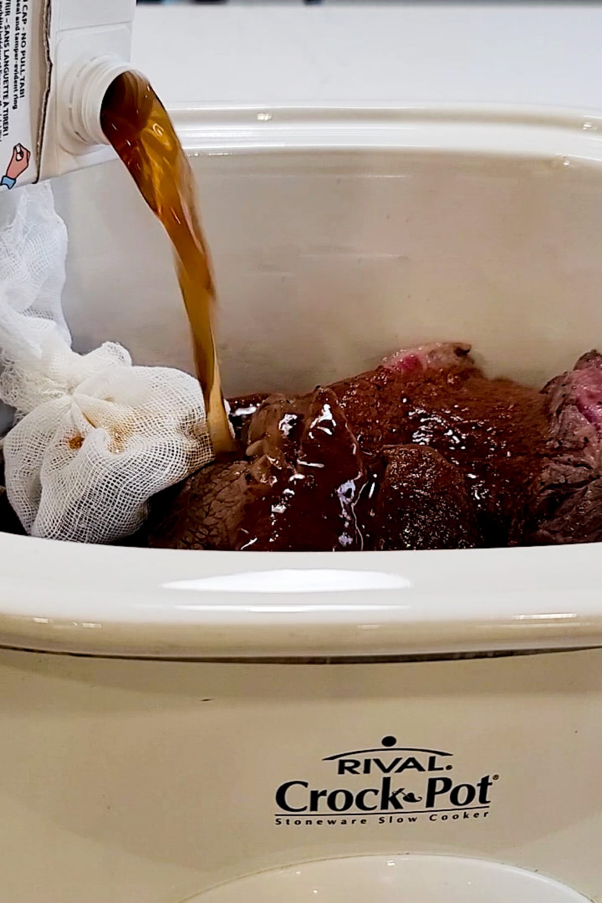 Beef broth being poured into a slow cooker for birria tacos.