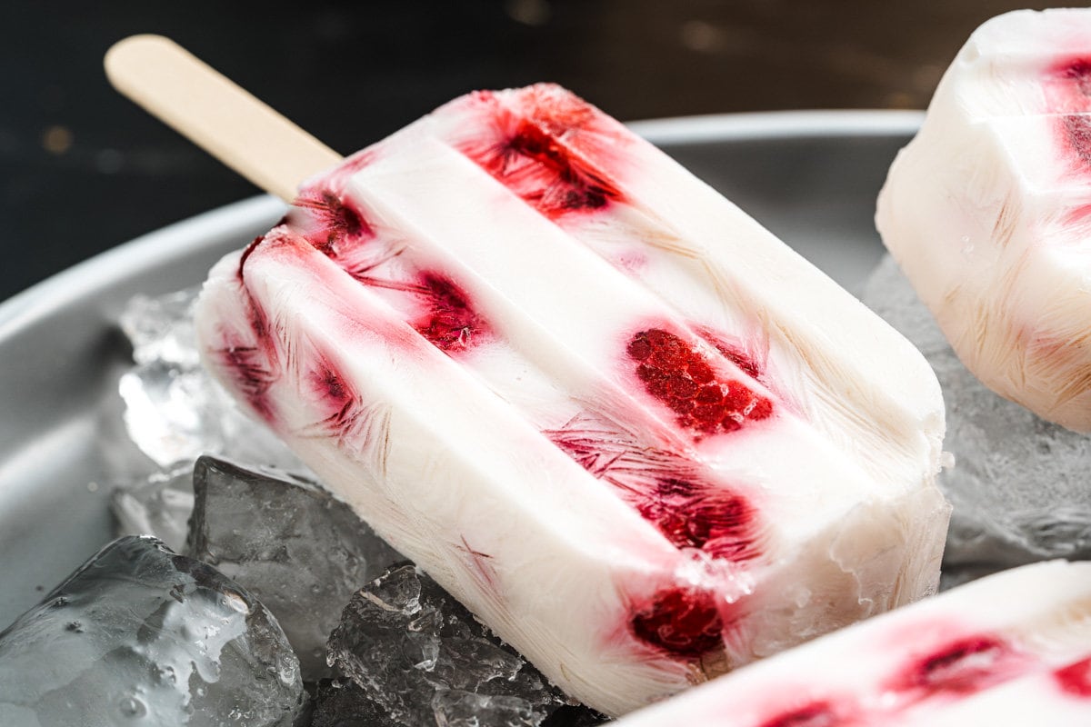 A Greek yogurt and raspberry popsicle on a plate filled with ice.