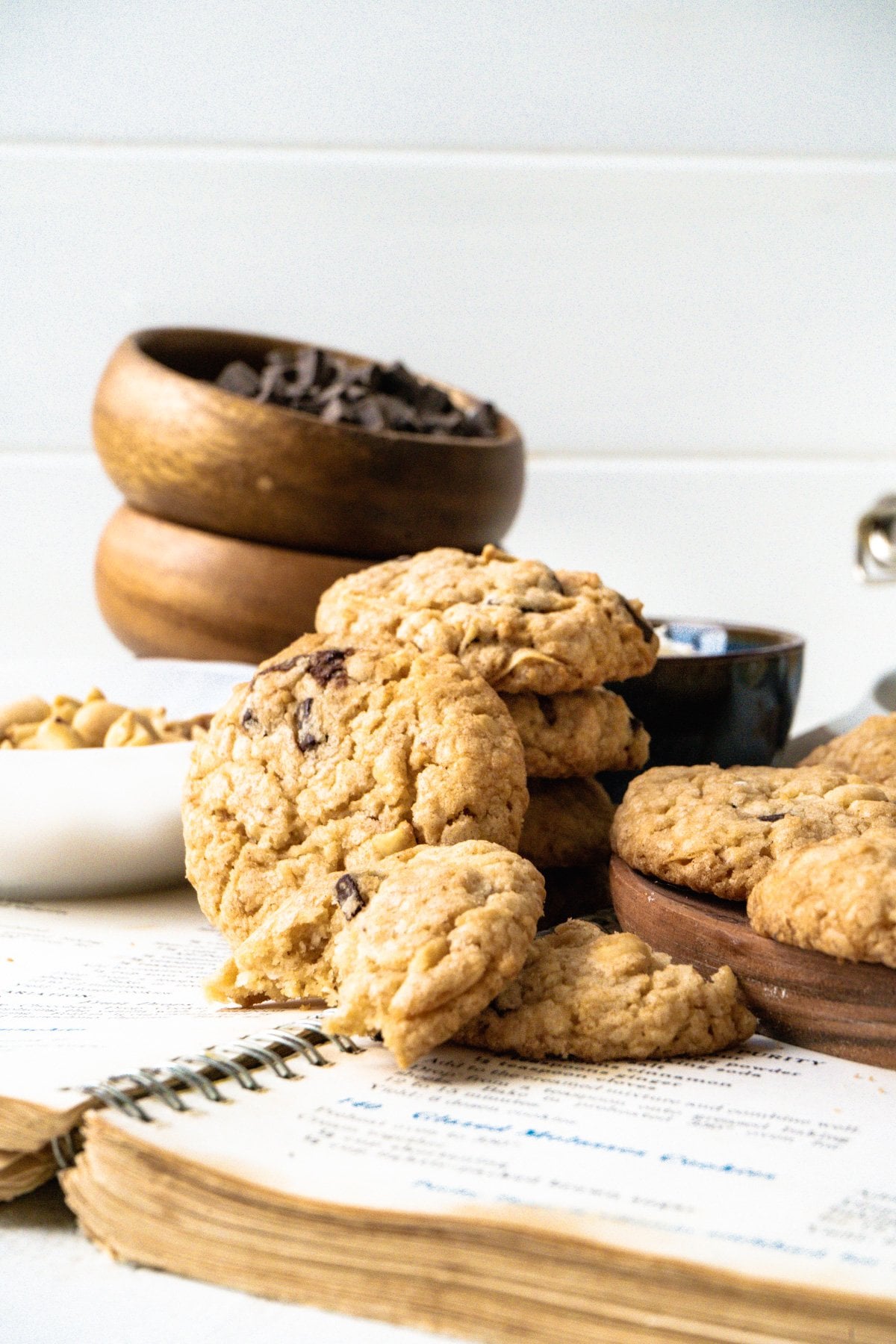 A pile of Everything But The Kitchen Sink Cookies on an open cookbook with baking supplies in the background.