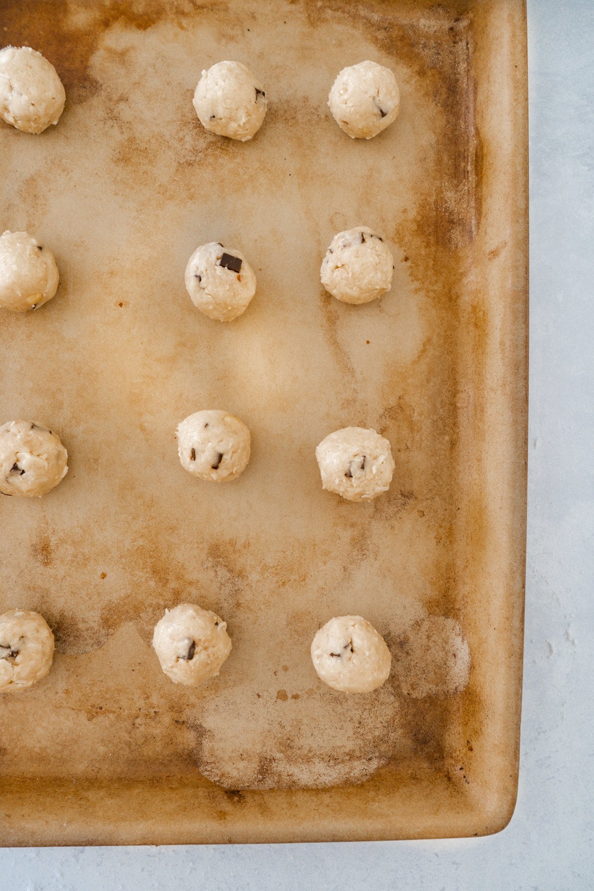 Chocolate chip oat and coconut cookies rolled into balls on a baking sheet ready to bake.