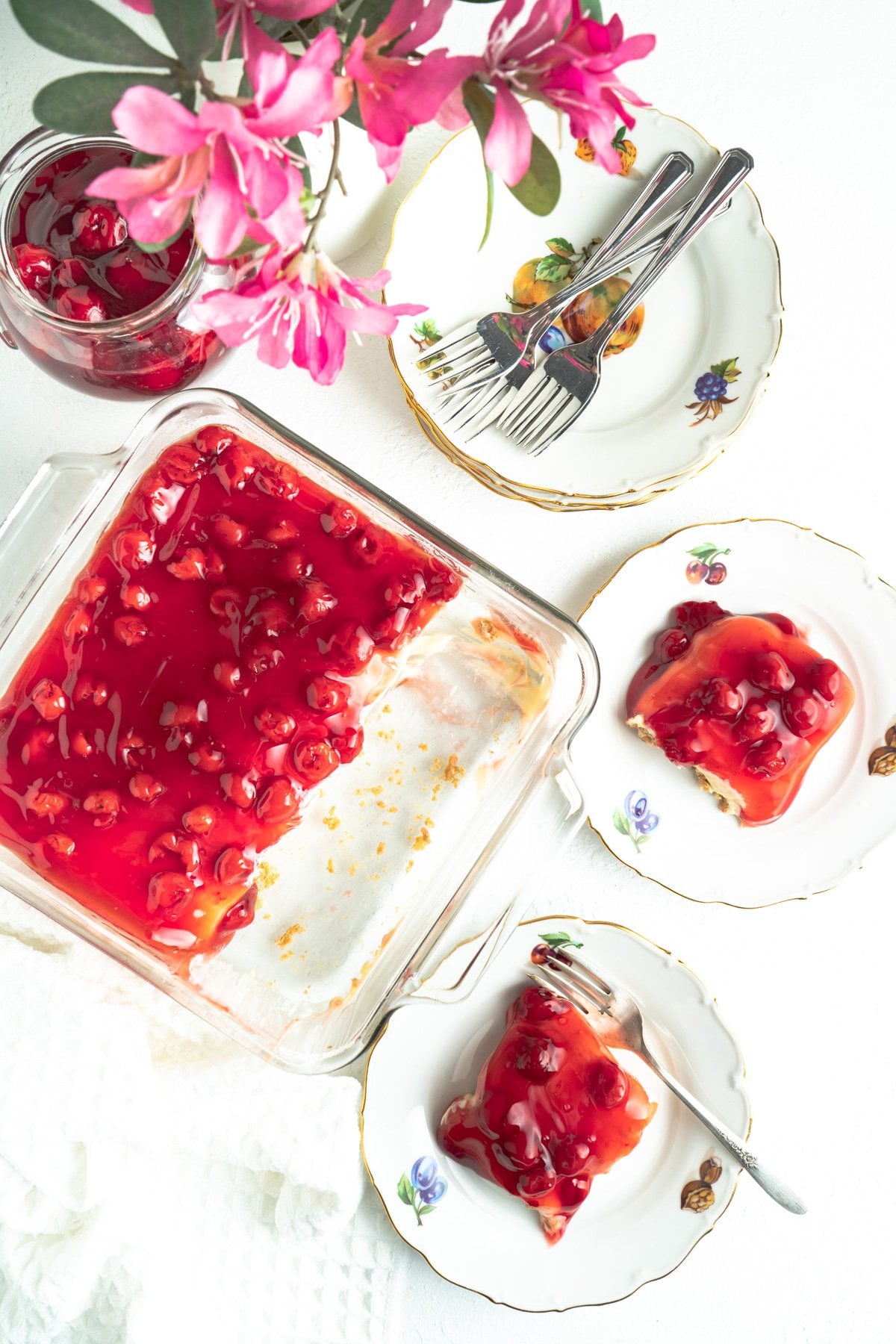 Plates of an easy no bake cherry cheesecakes on a table with the pan nearby.