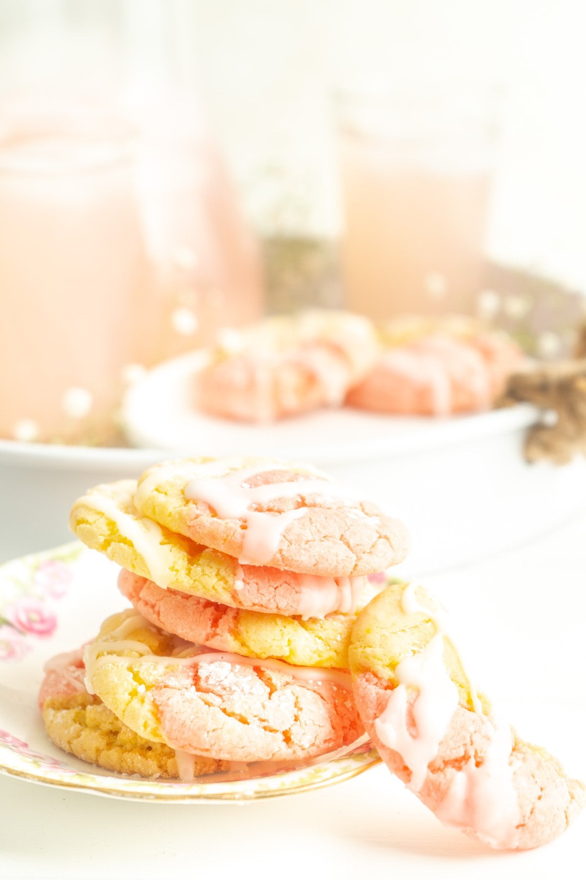 A stack of pink lemonade cookies on a white table with lemonade.