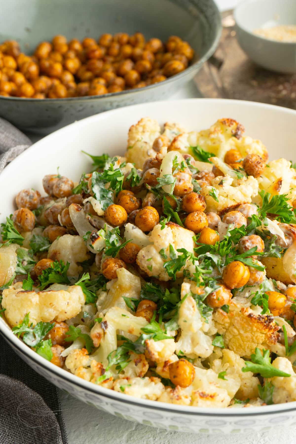 A cauliflower chickpea salad in a white bowl near a bowl of roasted chickpeas.