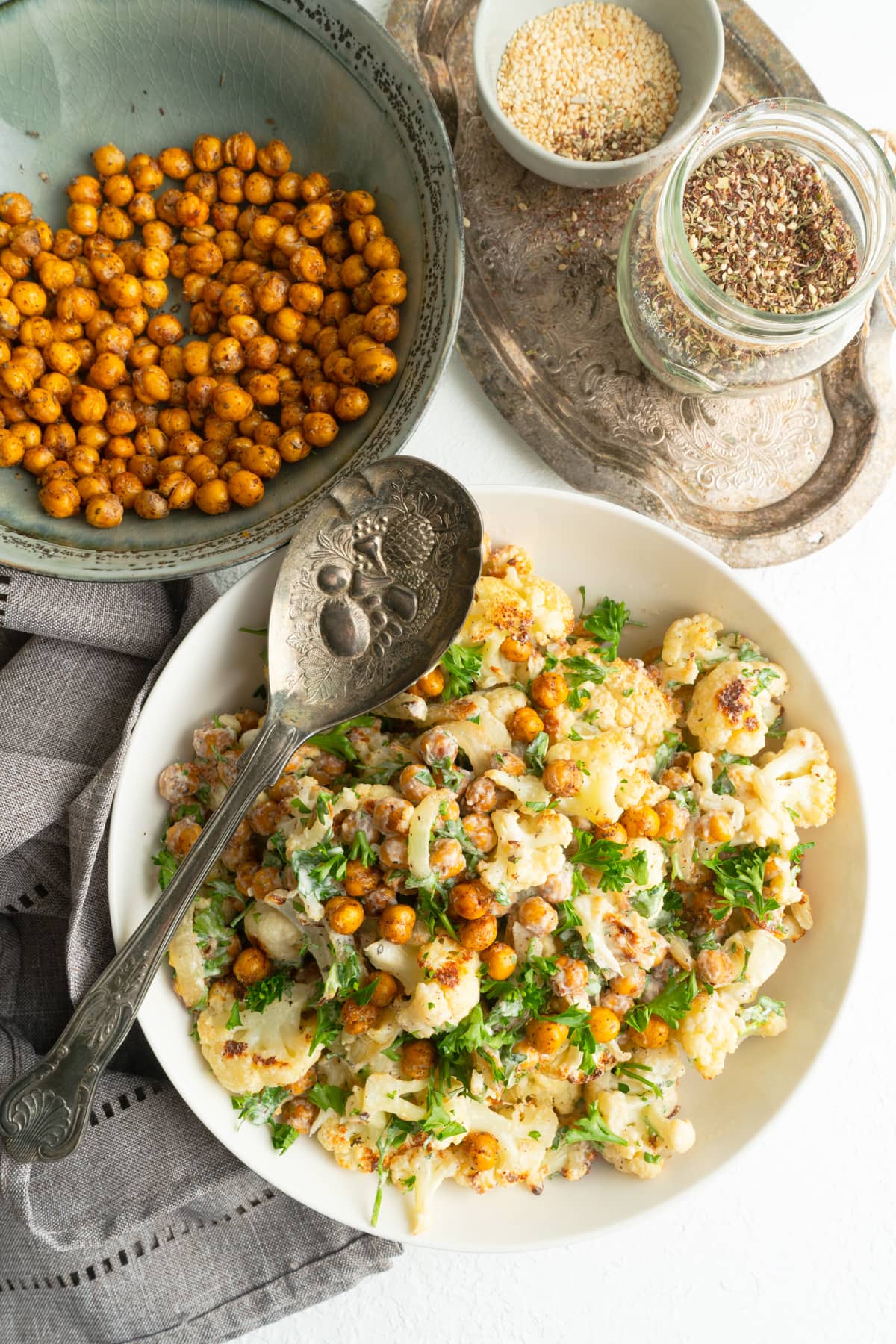 A Middle Eastern Cauliflower salad in a bowl with a spoon and some roasted chickpeas nearby.