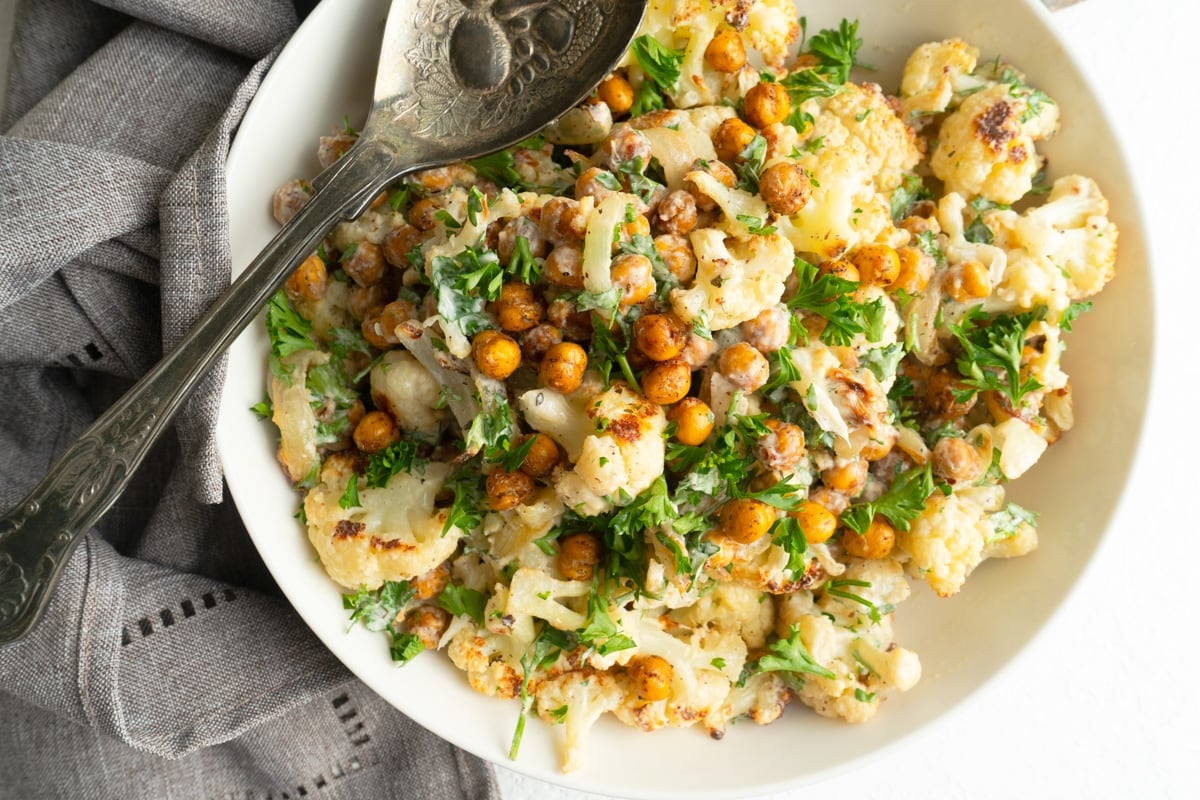 A Cauliflower and tahini salad in a white bowl with a spoon on a grey napkin.