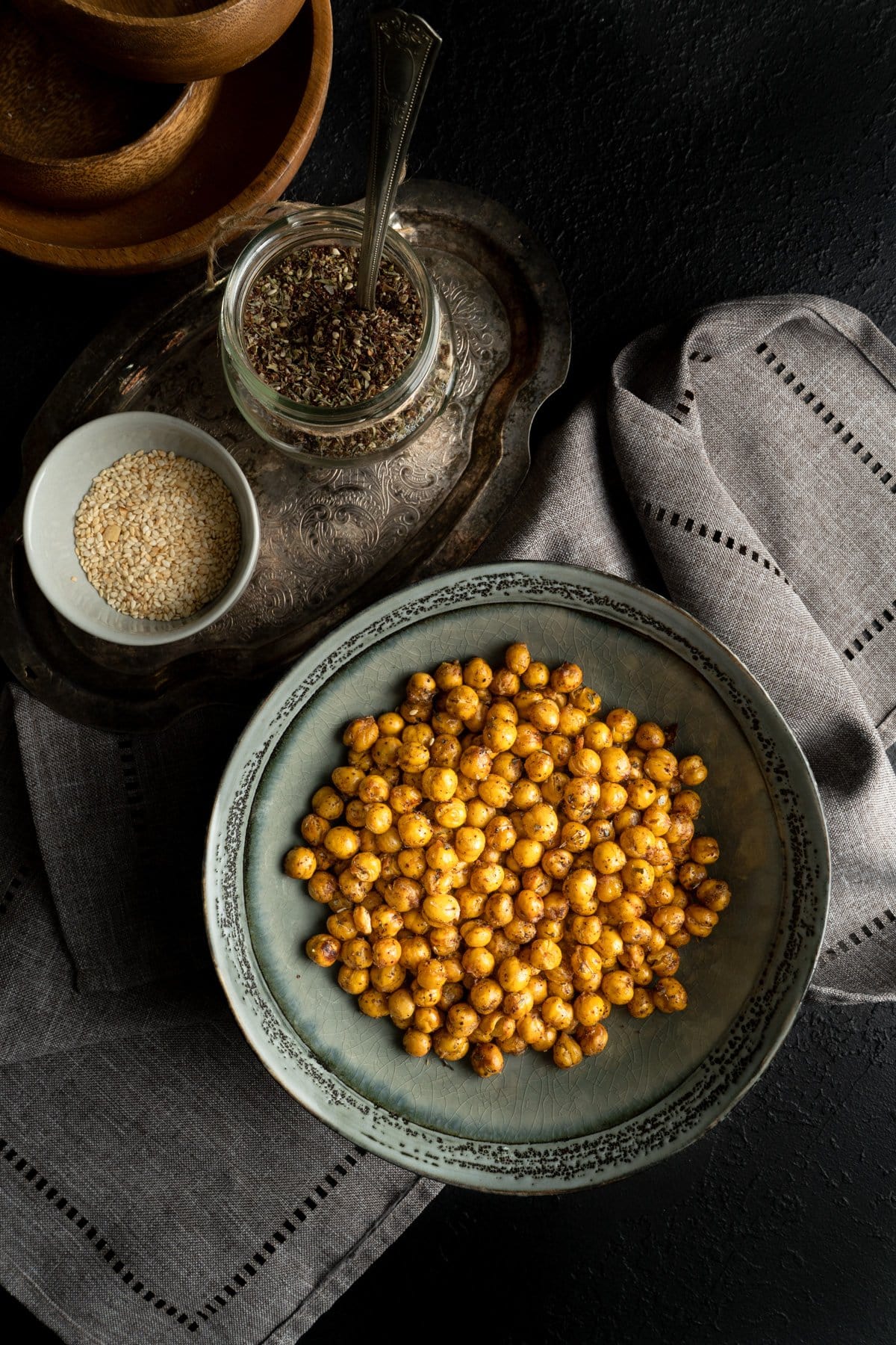 A fried chickpeas recipe in a grey bowl on a dark table with spices in a small bottle near and a grey napkin.