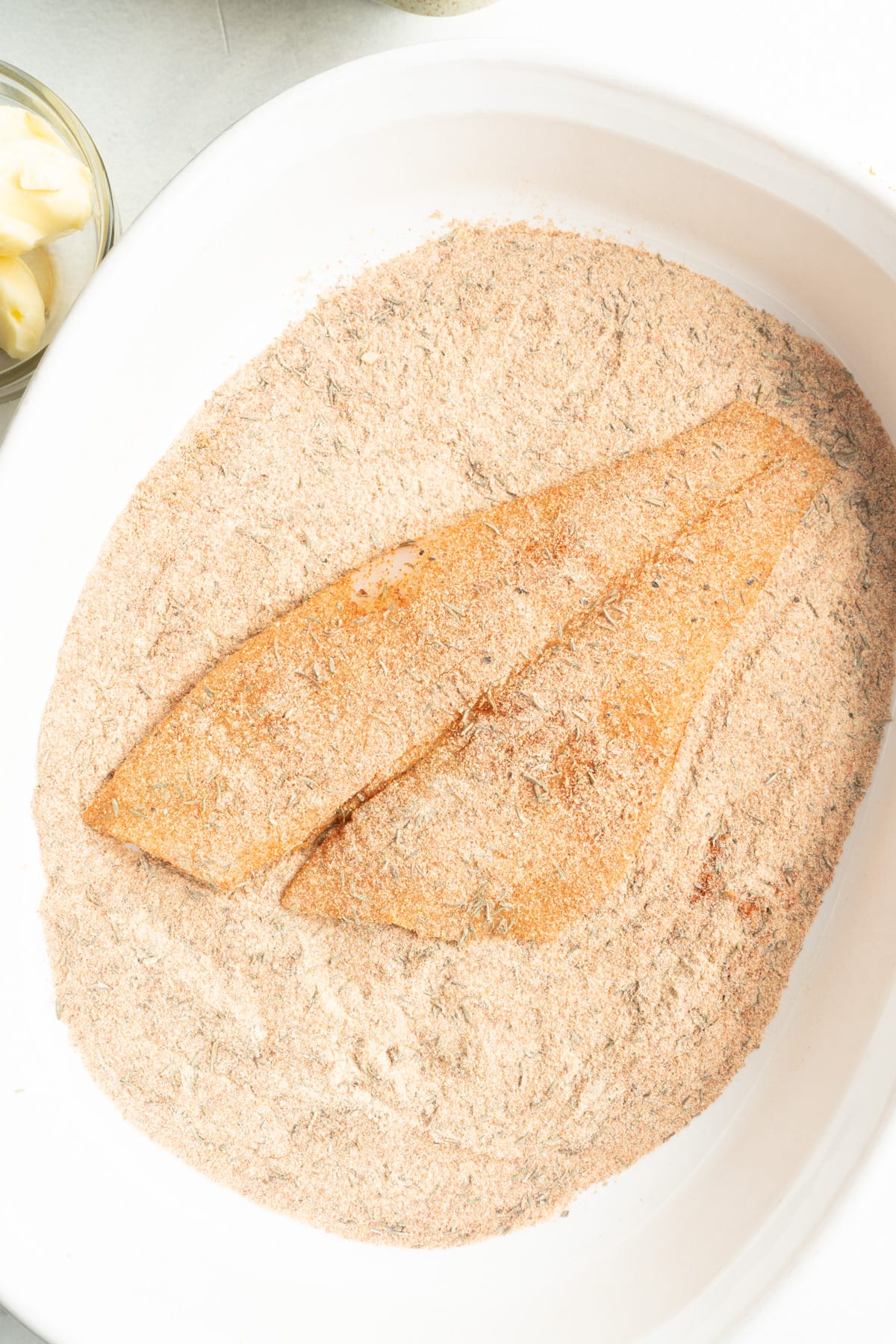 A filet of cod in a bowl filled with seasoning for blackened fish recipe.