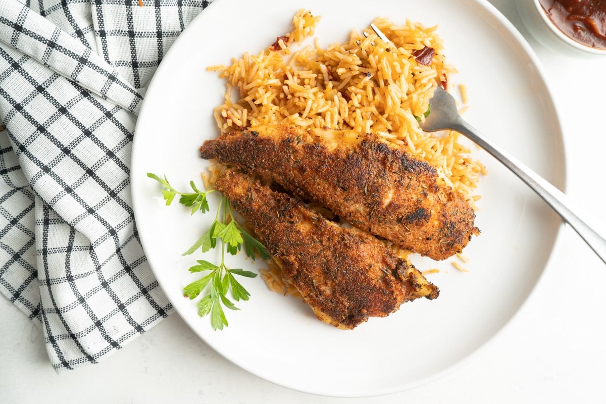 A plate with a blackened cod fillet and rice.